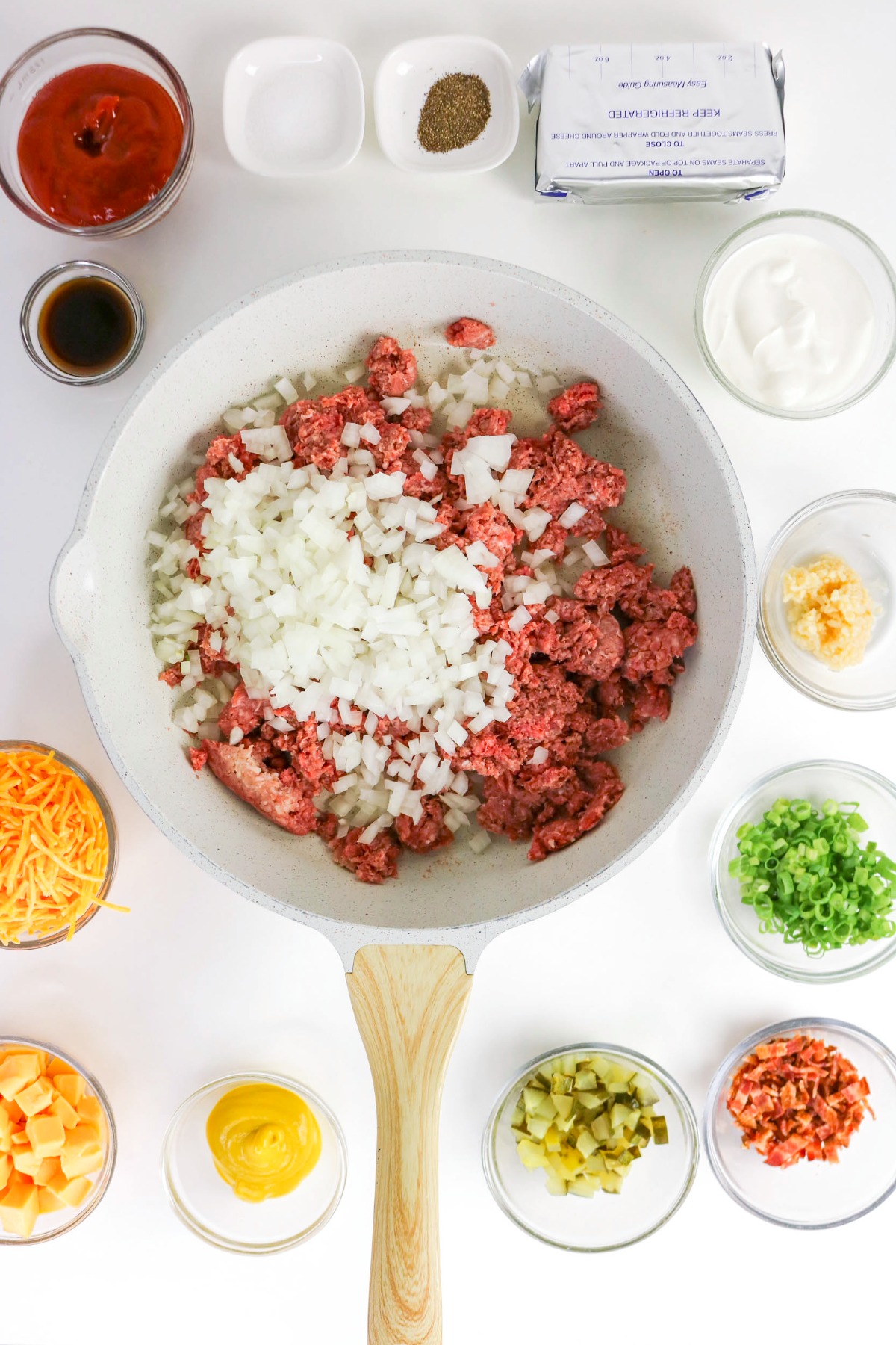 Ground beef in a large skillet cooking with diced onion.