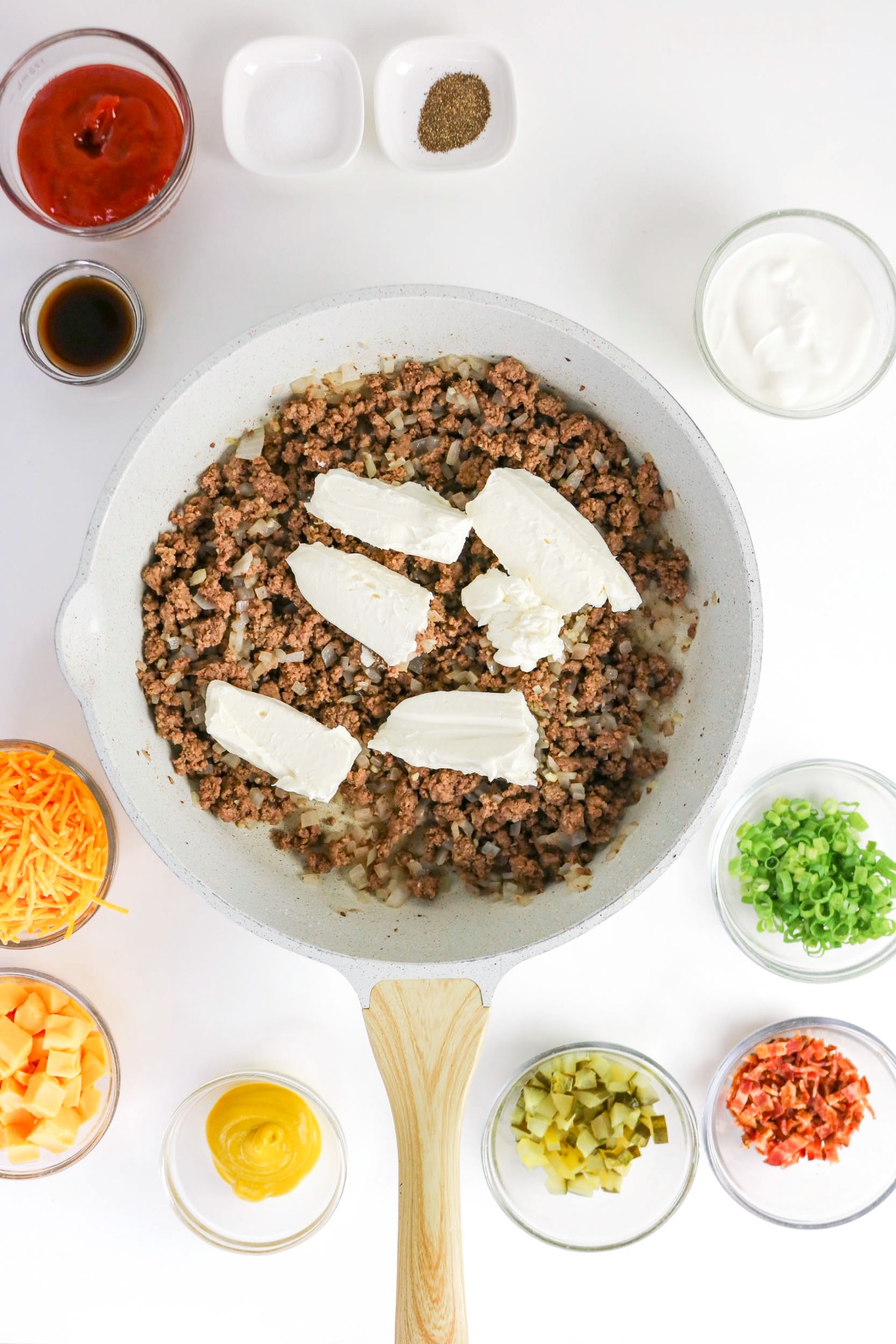 Block of cream cheese with cooked ground beef in a skillet.