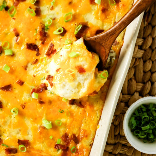 Twice baked potato casserole in a white baking dish with a wooden spoon taking a scoop out.