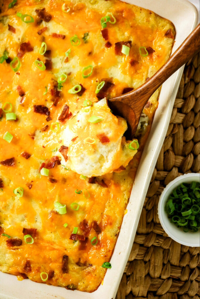Twice baked potato casserole in a white baking dish with a wooden spoon taking a scoop out.