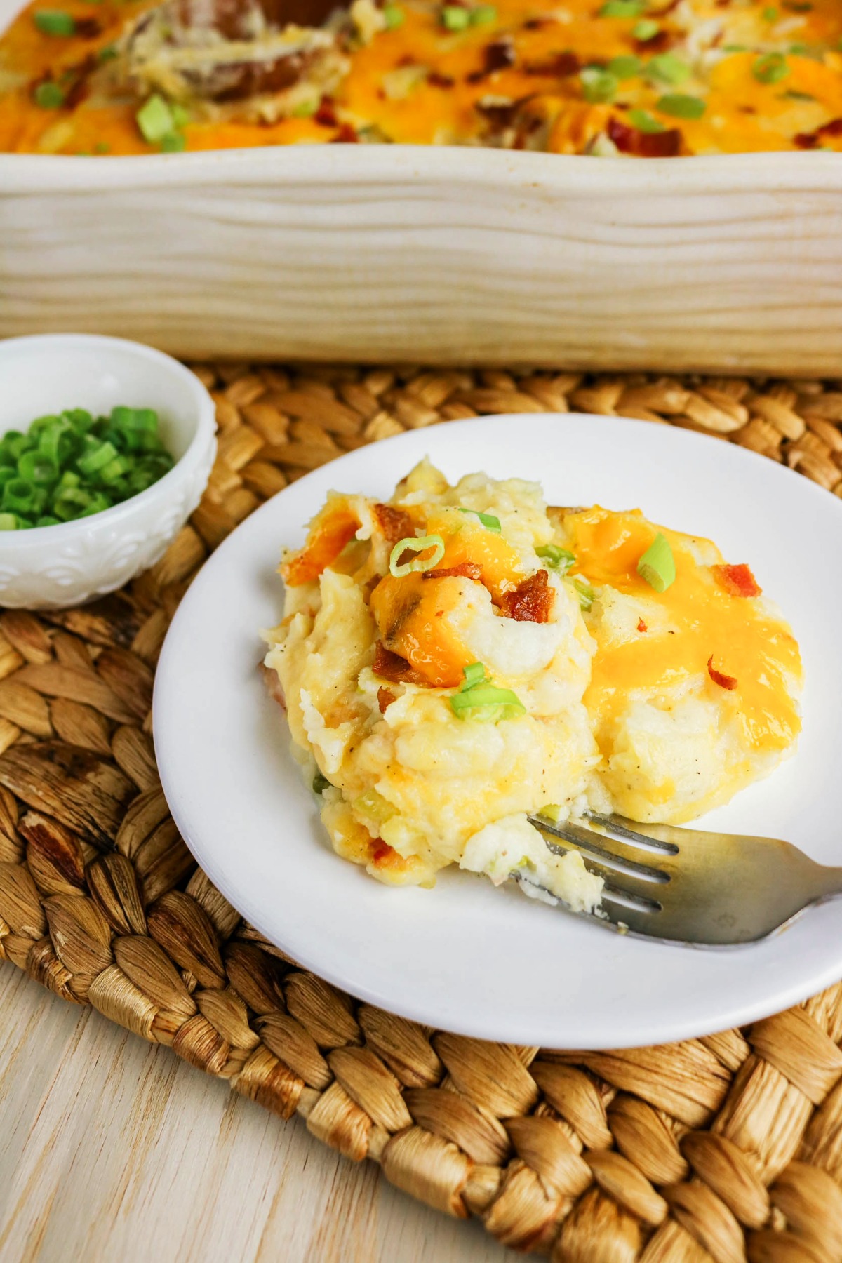 A scoop of twice baked mashed potatoes on a white plate with a fork on the side.
