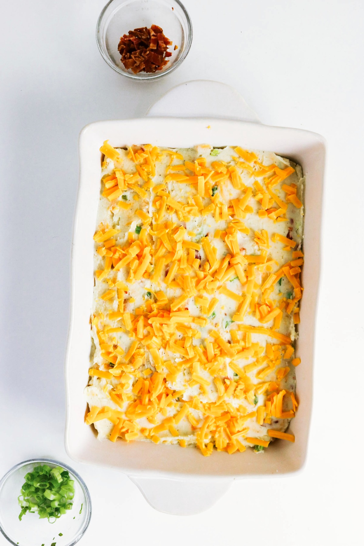 Twice baked mashed potatoes in a casserole dish topped with cheese before baking.