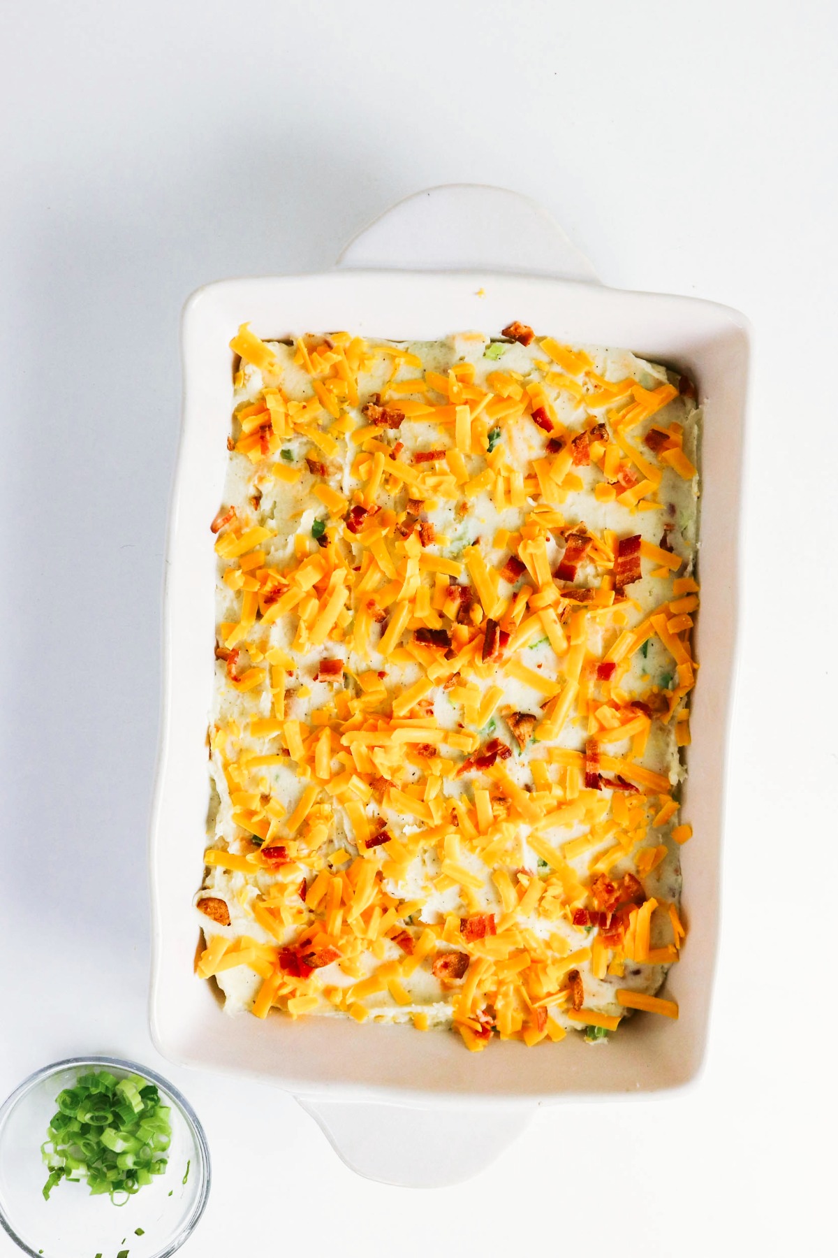 Mashed potato casserole dish topped with cheese and bacon before baking.