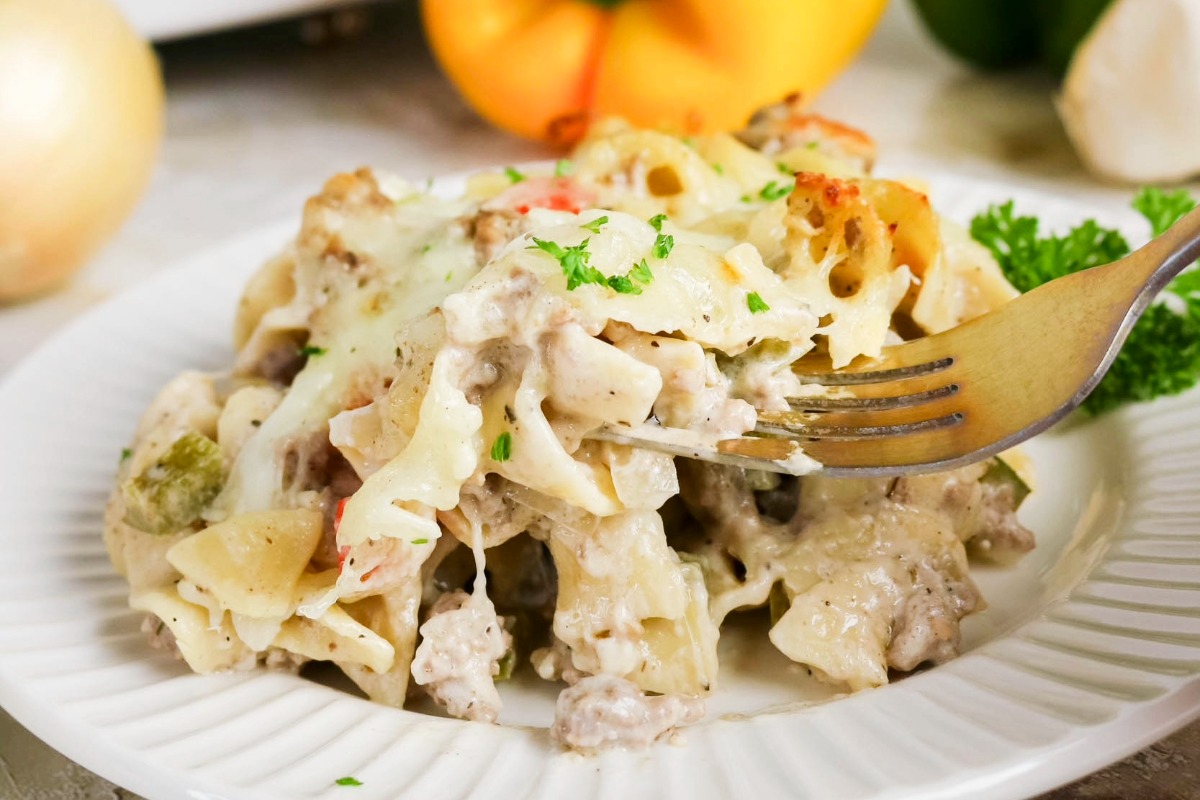 A serving of noodle casserole on a white serving plate with a fork ready to take a bite.