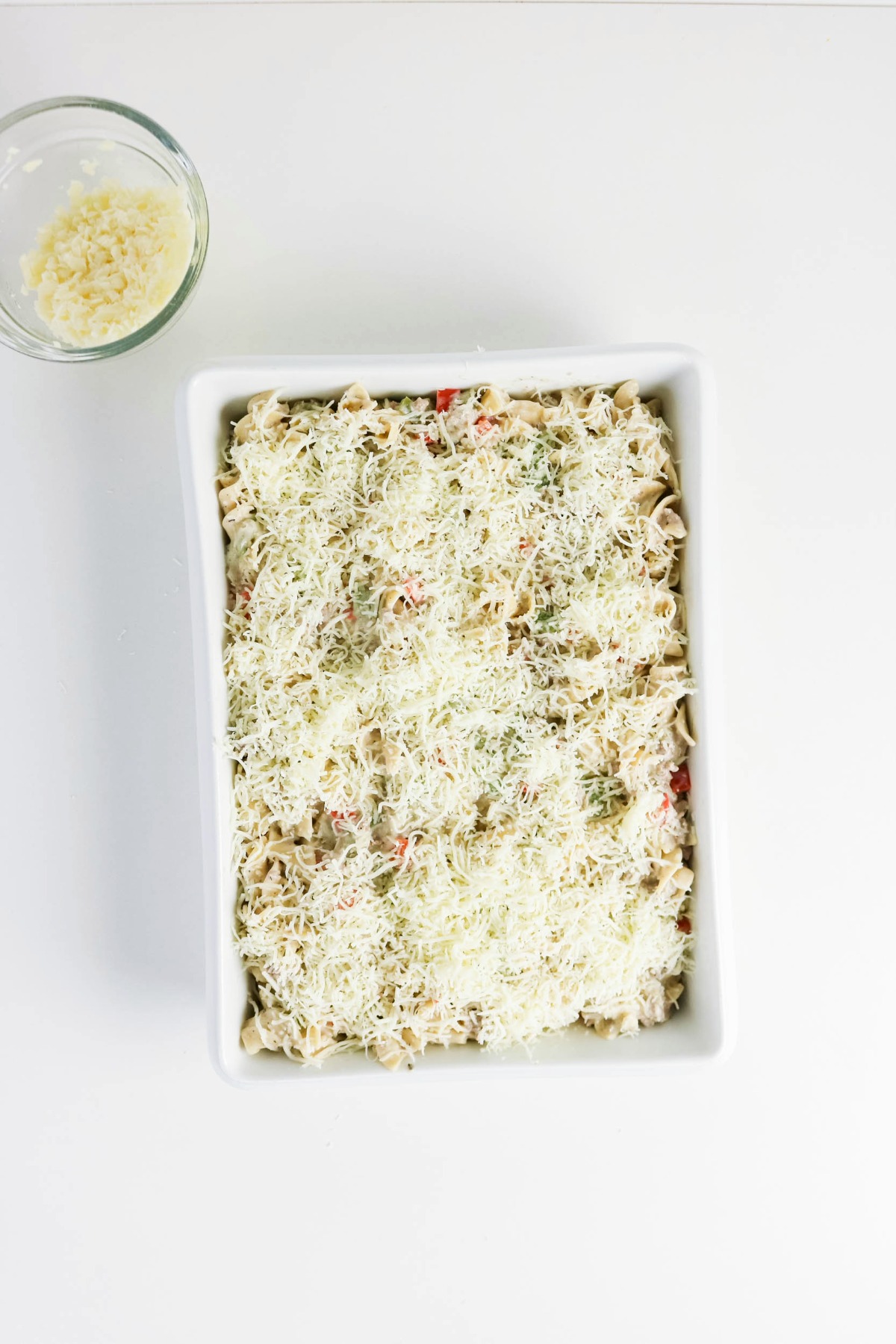 Noodle mixture in a casserole dish topped with shredded cheese before baking.