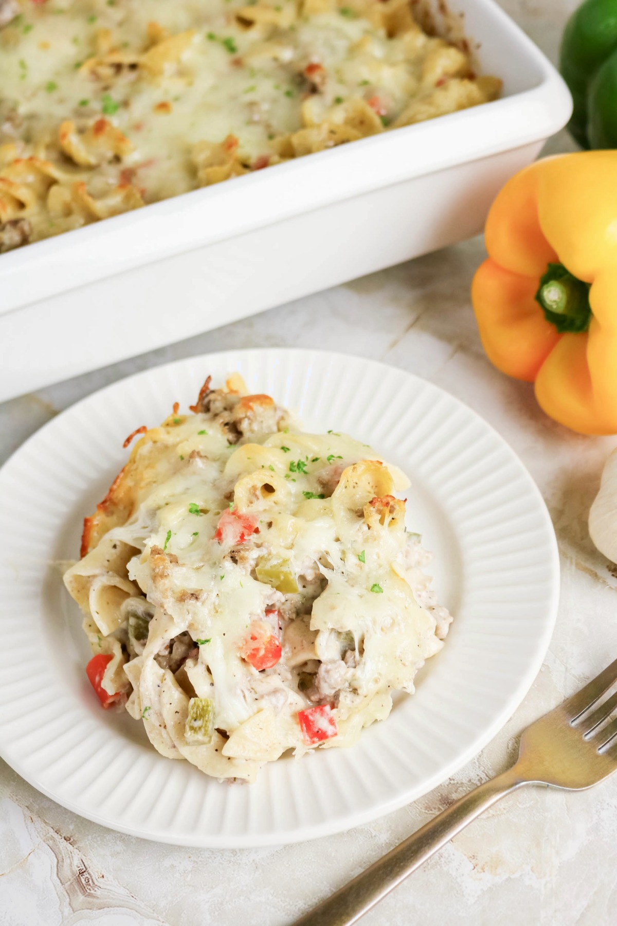 Overhead view of a casserole dish behind a plate with noodle casserole ready to eat.