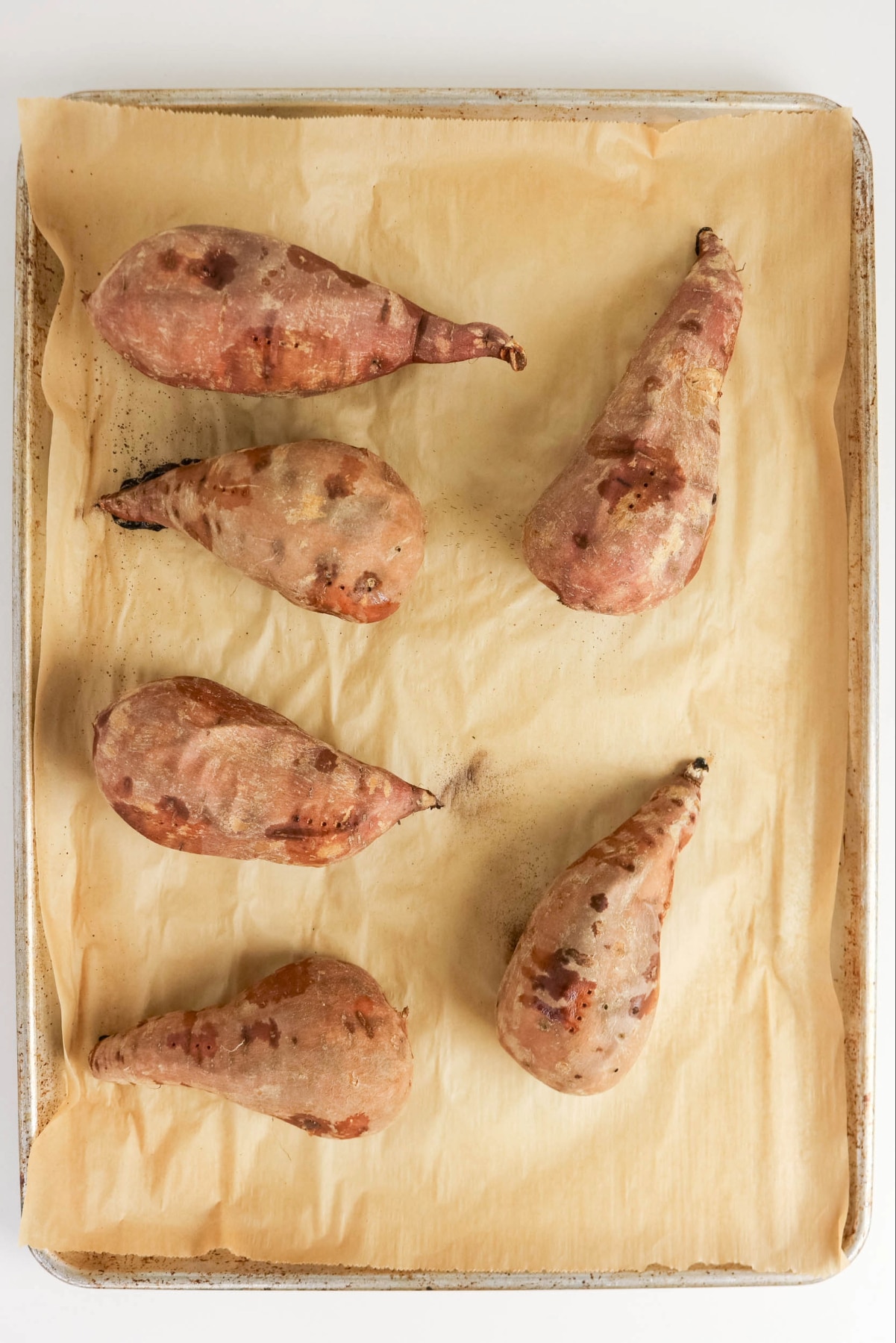 Whole sweet potatoes on a parchment lined baking sheet.