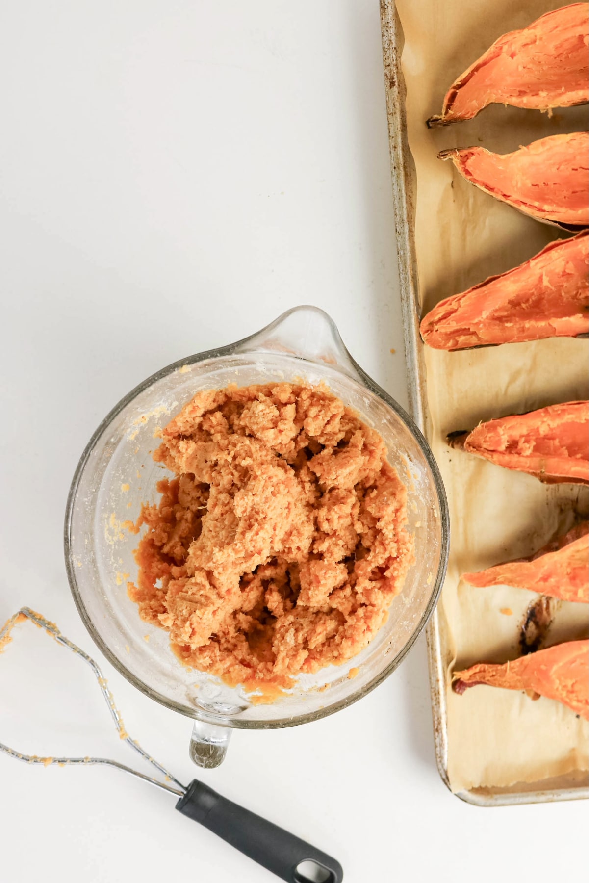 Sweet potato mix in a clear mixing bowl with potato shells on the side.