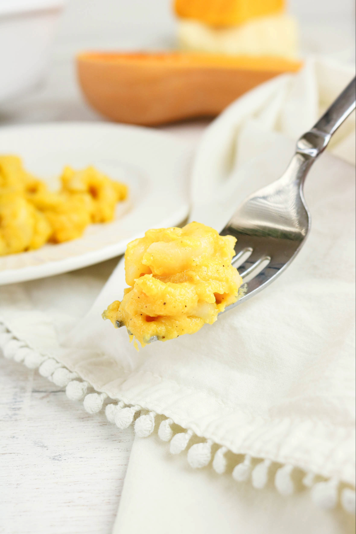 A forkful of macaroni and cheese with sliced butternut squash in the background.