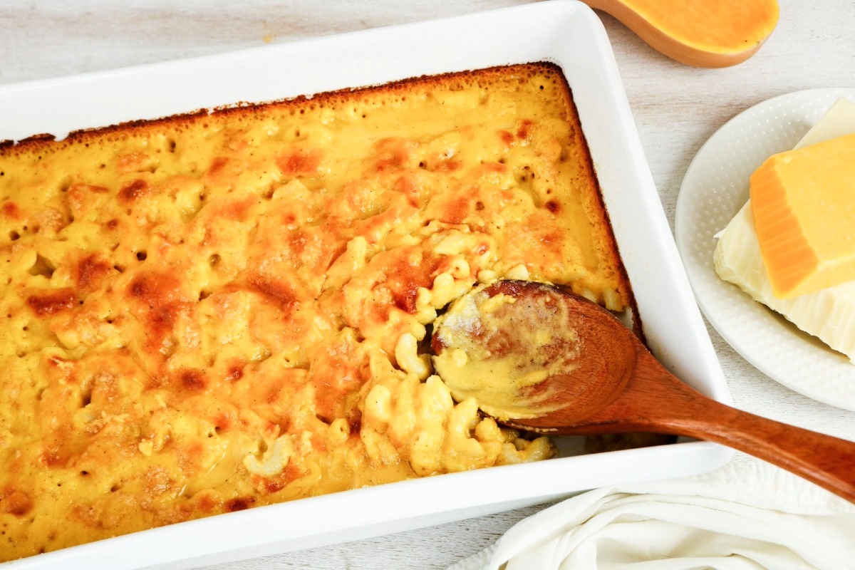 Mac and cheese in a white casserole baking dish with wooden spoon scooping out a portion.