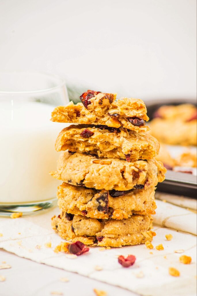 A stack of cranberry oatmeal cookies next to a glass of milk.