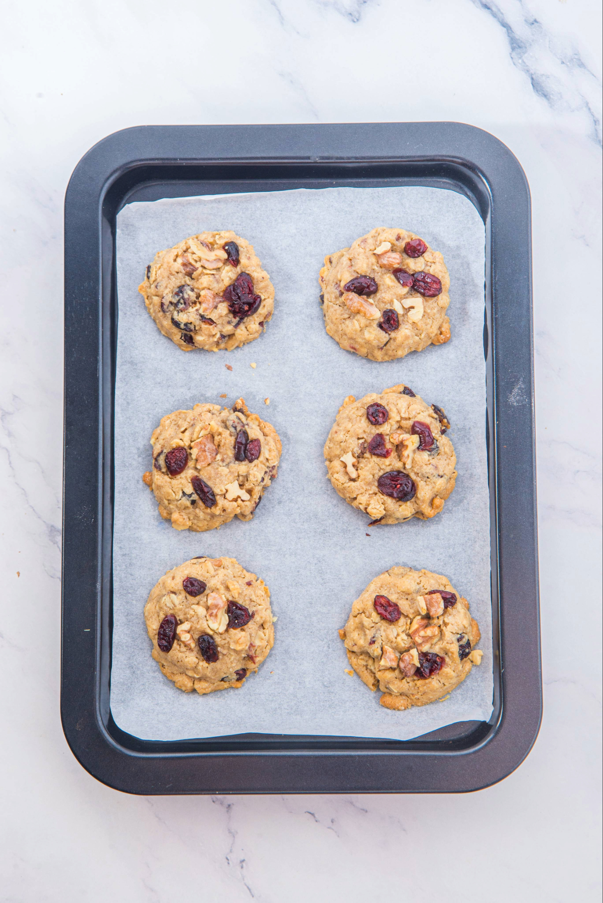 Baked cranberry oatmeal cookies on a baking sheet before placing on a cooling rack.