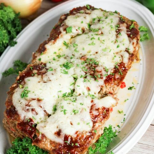 Whole meatloaf on a white platter with parsley before cutting.