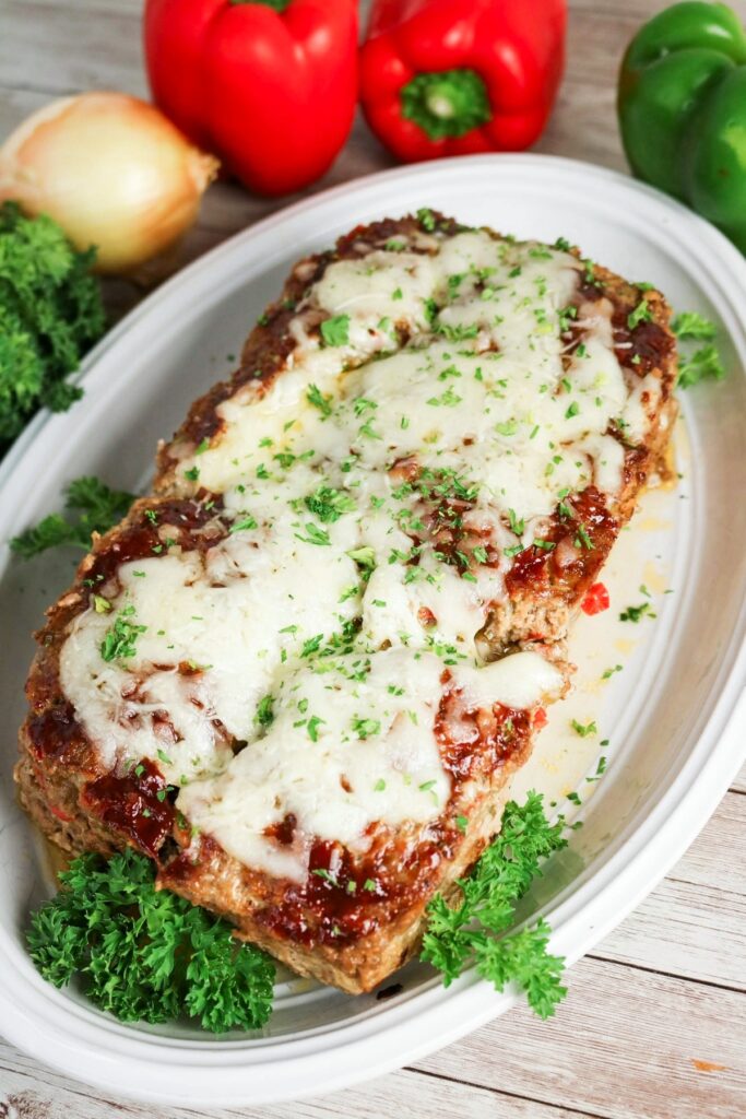 Whole meatloaf on a white platter with parsley before cutting.