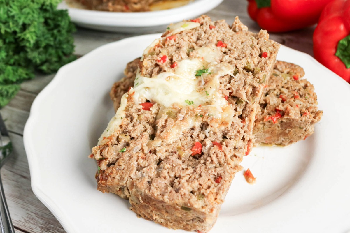 Sliced meatloaf with cheese oozing out of the middle on a white plate