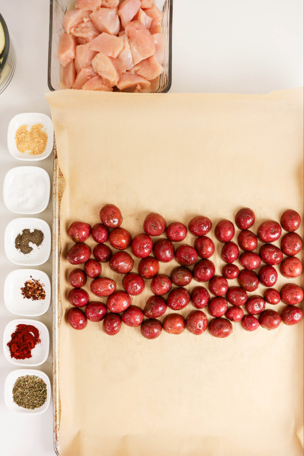 Seasoned potatoes cut in half and placed on a baking sheet before roasting.