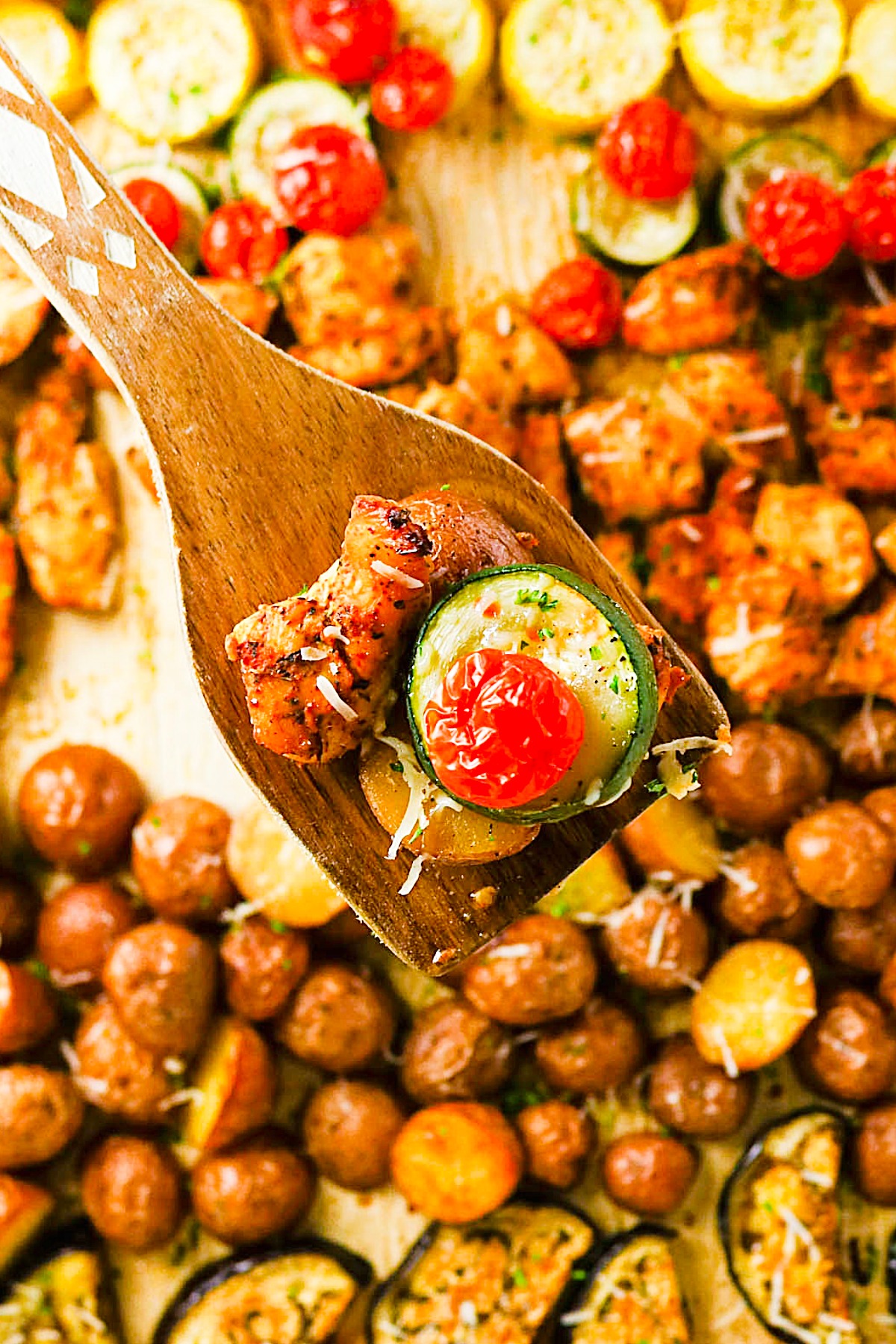 Wooden spatula with chicken and vegetables over a sheet pan.
