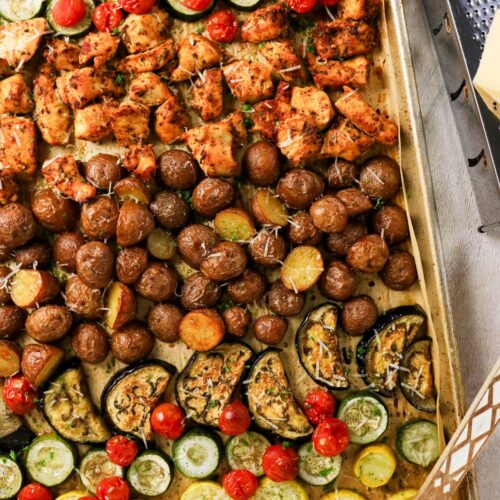 Roasted chicken and vegetables on a parchment lined baking sheet.