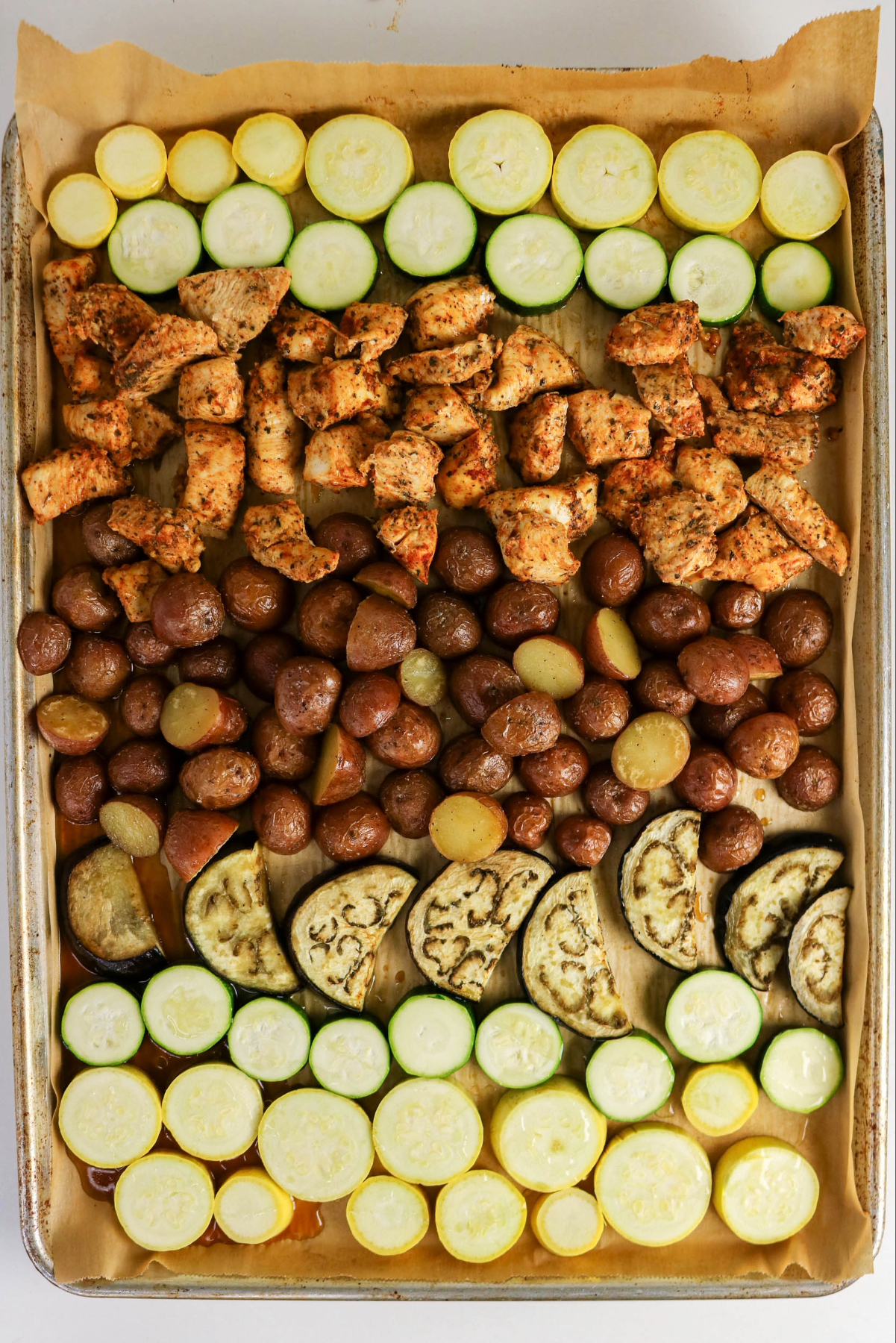 Sheet pan with partially cooked chicken and potatoes with vegetables.