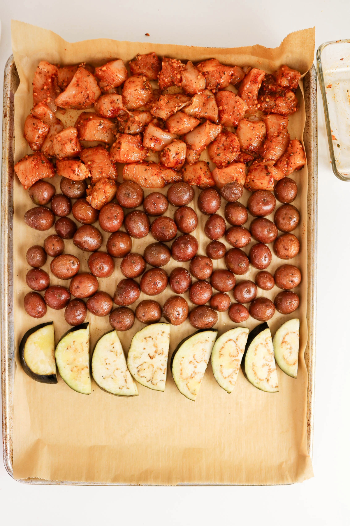 Seasoned diced chicken with partially cooked red potatoes on a baking sheet.
